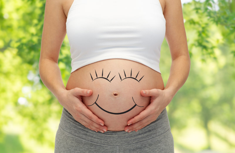 Mujer embarazada con cara sonriente pintada en la barriga